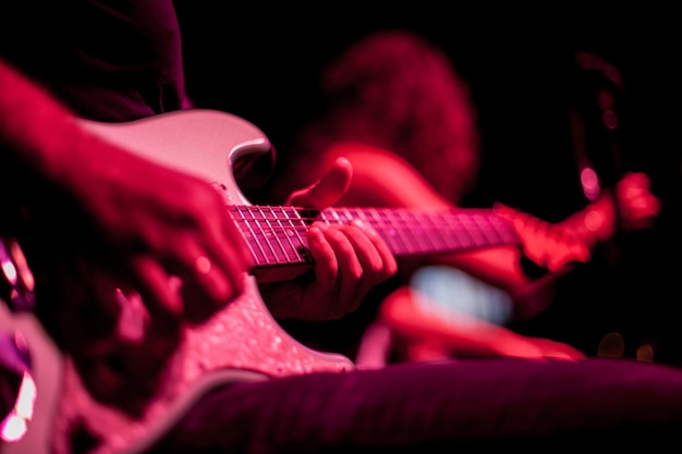 Guitarrista toca guitarra elétrica, close-up da guitarra e mãos, iluminação vermelha