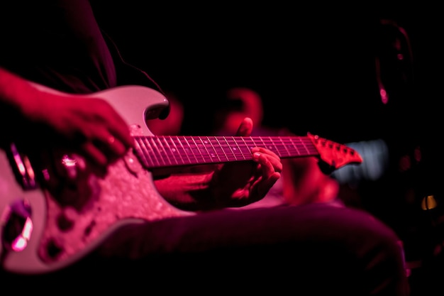 guitarrista toca guitarra elétrica, close-up da guitarra e mãos, iluminação vermelha