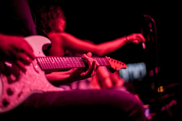 guitarrista toca guitarra elétrica, close-up da guitarra e mãos, iluminação vermelha