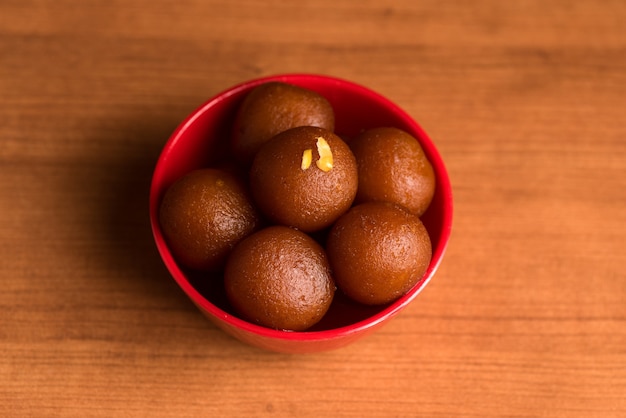 Gulab jamun em tigela vermelha na madeira. sobremesa indiana ou prato doce.