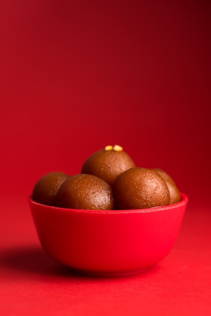 Gulab Jamun in roter Schale auf rot. Indisches Dessert oder süßes Gericht.