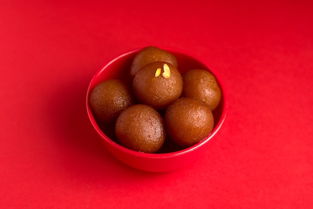 Gulab Jamun in roter Schale auf rot. Indisches Dessert oder süßes Gericht.