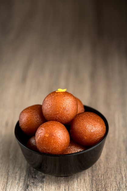 Gulab Jamun en un recipiente sobre fondo de madera.