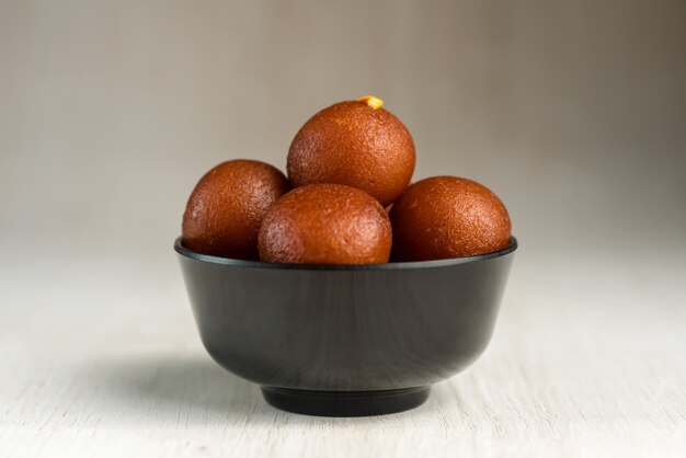 Gulab Jamun en un recipiente sobre fondo de madera.