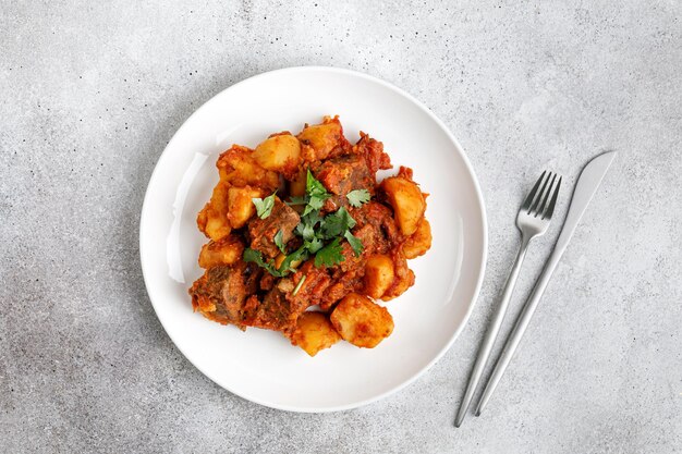 Gulasch-Rindereintopf mit Kartoffeln Geschmortes Fleisch mit grüner Petersilie auf weißem Teller Abendessen DishxA