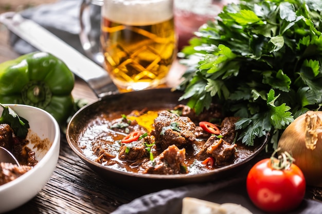 Gulasch serviert in einer Pfanne mit einem frischen Fassbier im Hintergrund.