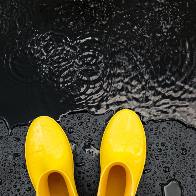 Gumboots amarelos brilhantes estão na chuva no preto