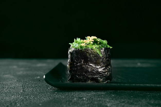 Foto gunkan maki sushi con algas hiyashi sobre una pizarra con jengibre y wasabi. cocina japonesa. entrega de comida. fondo negro