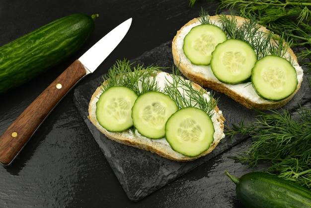 Gurkensandwiches ein Messer und eine frische Gurke und Dill auf einem schwarzen Hintergrund der Steinplatte