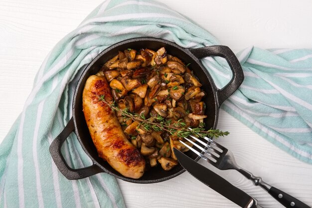 Gusseisenpfanne mit Bratwurst und Pilzen, flache Lage, Draufsicht.