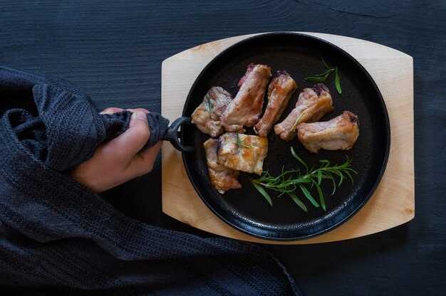 Gusseiserne schwarze runde Pfanne mit gebratenem Schweinefleisch auf schwarzem oder blauem Hintergrund, Ansicht von oben.