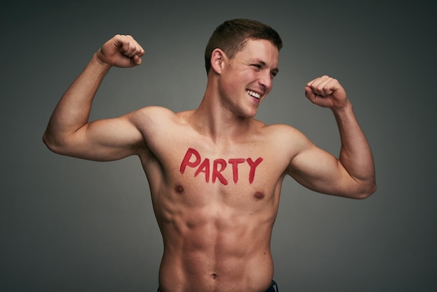 Le gusta la fiesta Foto de estudio de un joven alegre sin camisa parado y flexionando sus músculos con la palabra fiesta escrita en el pecho