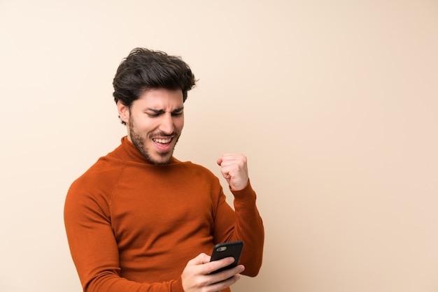 Gut aussehend über isolierte Mauer mit Telefon in Siegposition