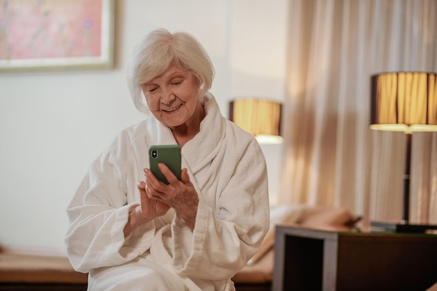 Gut aussehende ältere Frau im weißen Gewand mit einem Telefon in den Händen