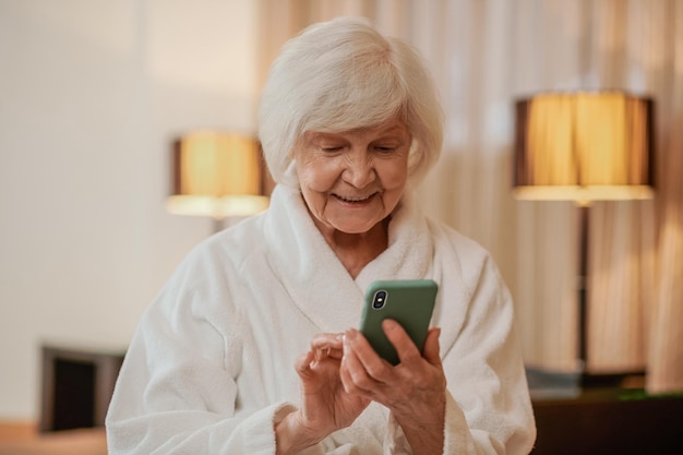 Gut aussehende ältere Frau im weißen Gewand mit einem Telefon in den Händen