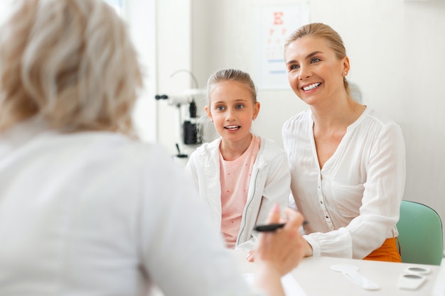 Gut aussehende blonde Mutter, die mit niedlichem kleinen Mädchen sitzt