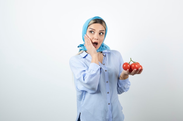 Gut aussehende Frau im blauen Schal, der rote frische Tomaten hält