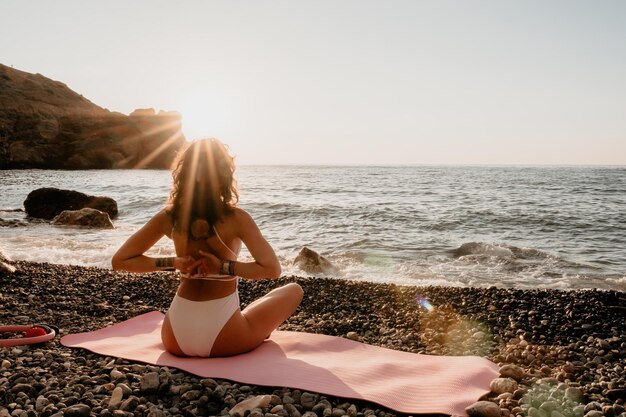 Gut aussehende Frau mittleren Alters in weißem Badeanzug und Armbändern im Boho-Stil, die im Freien auf einer Yogamatte am Meer bei Sonnenuntergang praktizieren Yoga-Fitness-Routine für Frauen Gesunder Lebensstil, Harmonie und Meditation