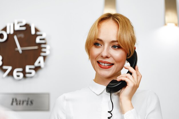 Gut aussehende freundliche Hotelrezeptionistin, die am Telefon Nahaufnahme spricht