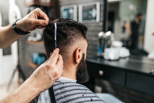 Gut aussehender bärtiger Mann, der Friseur im Friseursalon besucht.