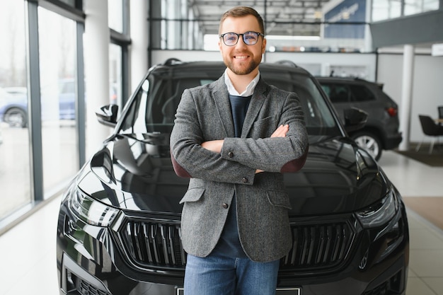 Gut aussehender, fröhlicher und freundlicher Verkäufer posiert in einem Autosalon oder Ausstellungsraum