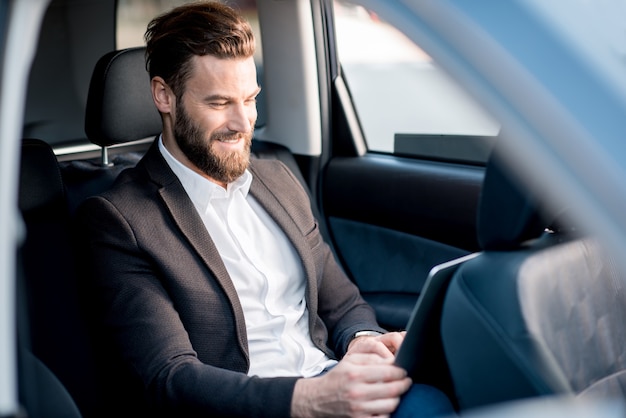 Gut aussehender Geschäftsmann, der mit Laptop auf dem Rücksitz des Autos sitzt