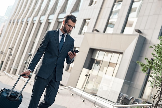 Gut aussehender junger Mann im vollen Anzug, der sein Smartphone benutzt, während