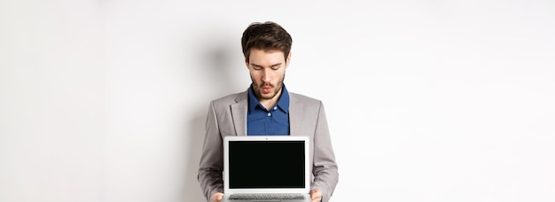 Gut aussehender kaukasischer Geschäftsmann im Anzug, der einen leeren Laptop-Bildschirm zeigt, demonstriert Promo, das auf whi steht