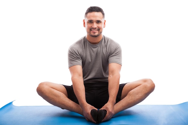 Gut aussehender lateinamerikanischer Typ, der auf einer Yogamatte sitzt und einige Dehnübungen auf weißem Hintergrund macht