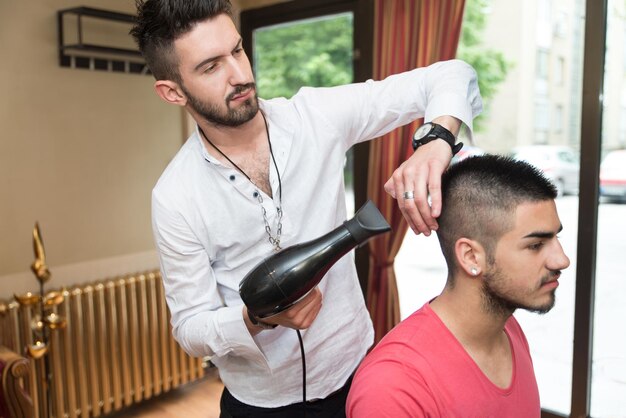 Gut aussehender Mann beim Friseur, der sein Haar föhnt