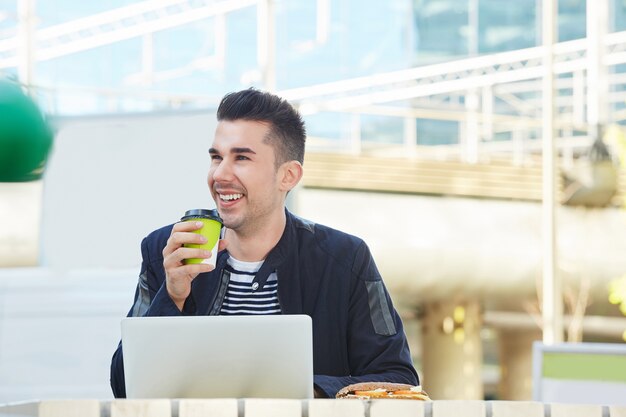 Gut aussehender Mann, der an Laptop Café am im Freien mit Kaffee arbeitet