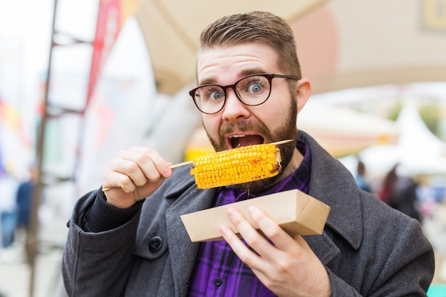 Foto gut aussehender mann, der auf der straße gerösteten mais isst.