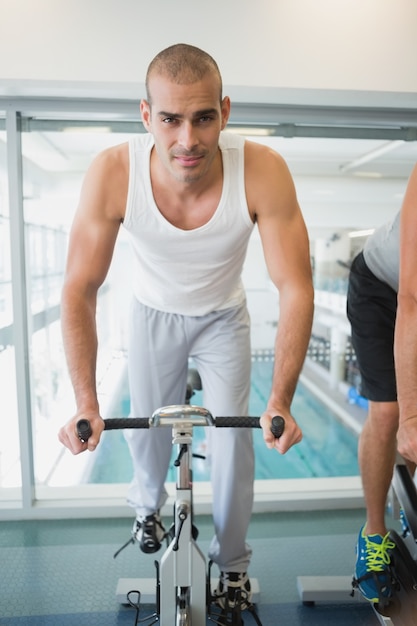 Gut aussehender Mann, der auf Hometrainer an der Turnhalle ausarbeitet