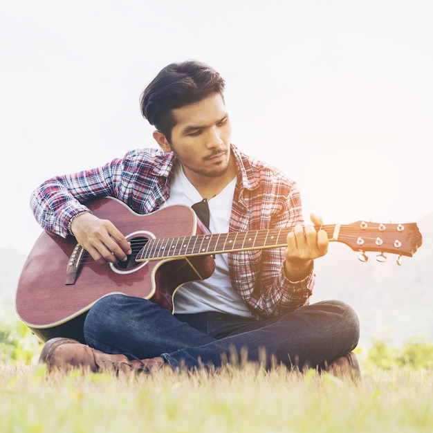 Gut aussehender Mann, der Gitarre auf grünem Gras spielt