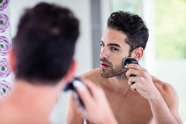 Gut aussehender Mann, der im Spiegel im Badezimmer sich rasiert
