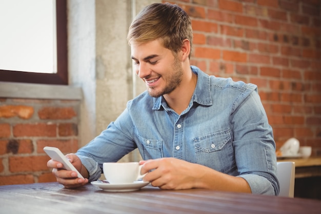 Gut aussehender Mann, der Kaffee trinkt und Smartphone verwendet