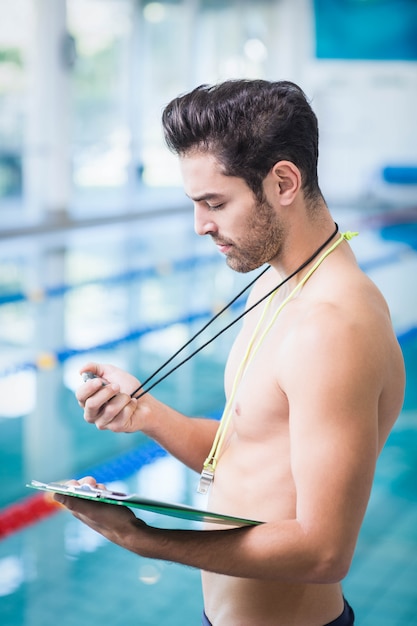 Gut aussehender Mann, der Klemmbrett und Stoppuhr am Pool hält