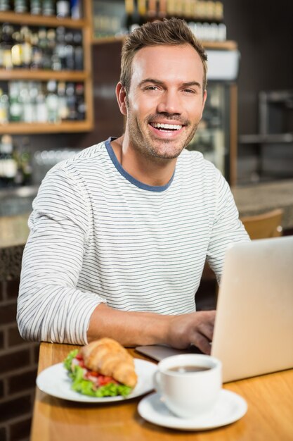 Gut aussehender Mann, der Laptop verwendet und ein Hörnchen isst