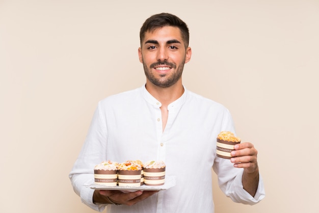 Gut aussehender Mann, der Muffinkuchen über lokalisierter Wand hält