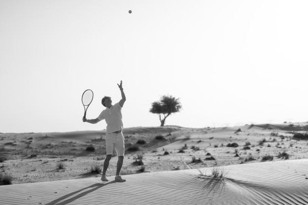 Gut aussehender Mann, der Tennis auf einem Barkhan in der Wüste spielt. Sonnenuntergang. Sport. Gerichte