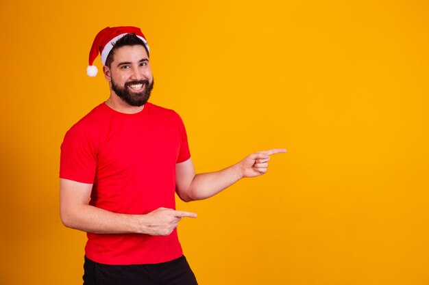 Gut aussehender Mann gekleidet zu Weihnachten mit Weihnachtsmann-Hut, der auf freien Textraum zeigt. Jahresabschlussaktion