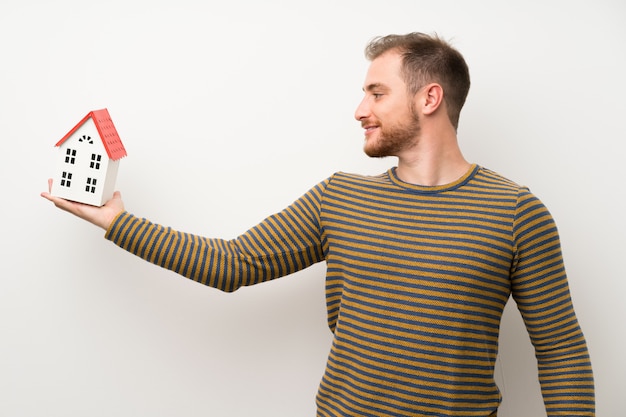 Gut aussehender Mann lokalisierte die weiße Wand, die ein kleines Haus hält