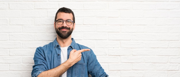 Gut aussehender Mann mit Bart über weißer Backsteinmauer Finger auf die Seite zeigend