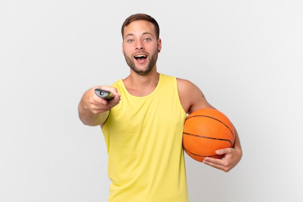 Gut aussehender Mann mit Basketballball und Auswahl eines Kanals mit einem Controller