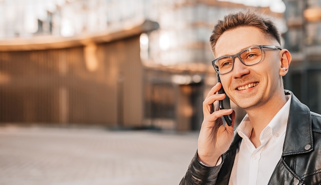 Gut aussehender Mann mit Brille mit einem Smartphone auf der Straße einer Großstadt. Geschäftsmann, der auf städtischem Hintergrund telefoniert