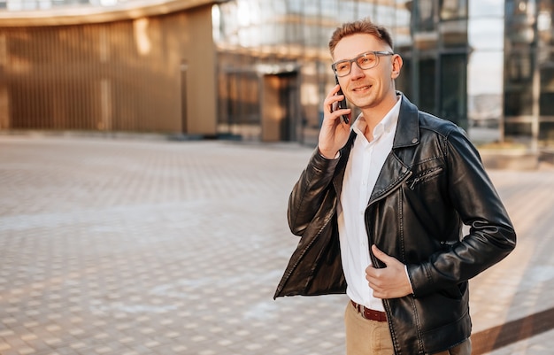 Gut aussehender Mann mit Brille mit einem Smartphone auf der Straße einer Großstadt. Geschäftsmann, der auf städtischem Hintergrund telefoniert