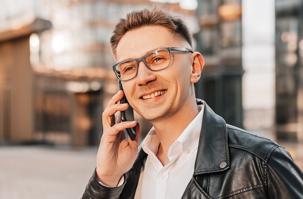 Gut aussehender Mann mit Brille mit einem Smartphone auf der Straße einer Großstadt. Geschäftsmann, der auf städtischem Hintergrund telefoniert