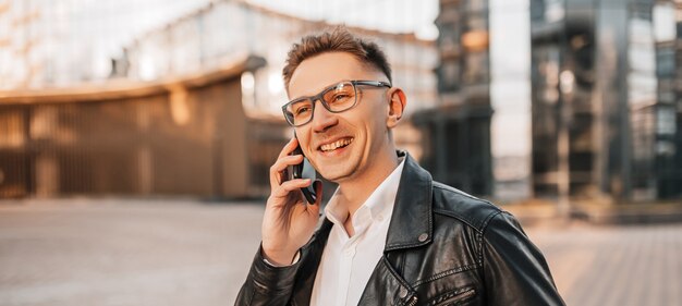 Gut aussehender Mann mit Brille mit einem Smartphone auf der Straße einer Großstadt. Geschäftsmann, der auf städtischem Hintergrund telefoniert