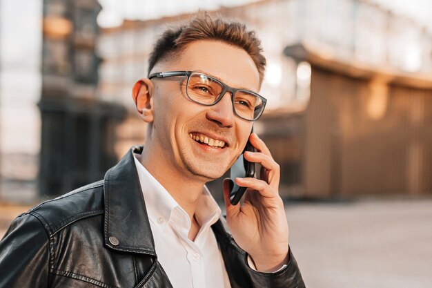 Gut aussehender Mann mit Brille mit einem Smartphone auf der Straße einer Großstadt. Geschäftsmann, der auf städtischem Hintergrund telefoniert