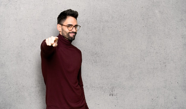 Gut aussehender Mann mit Brille zeigt Finger auf Sie mit einem überzeugten Ausdruck über strukturierter Wand